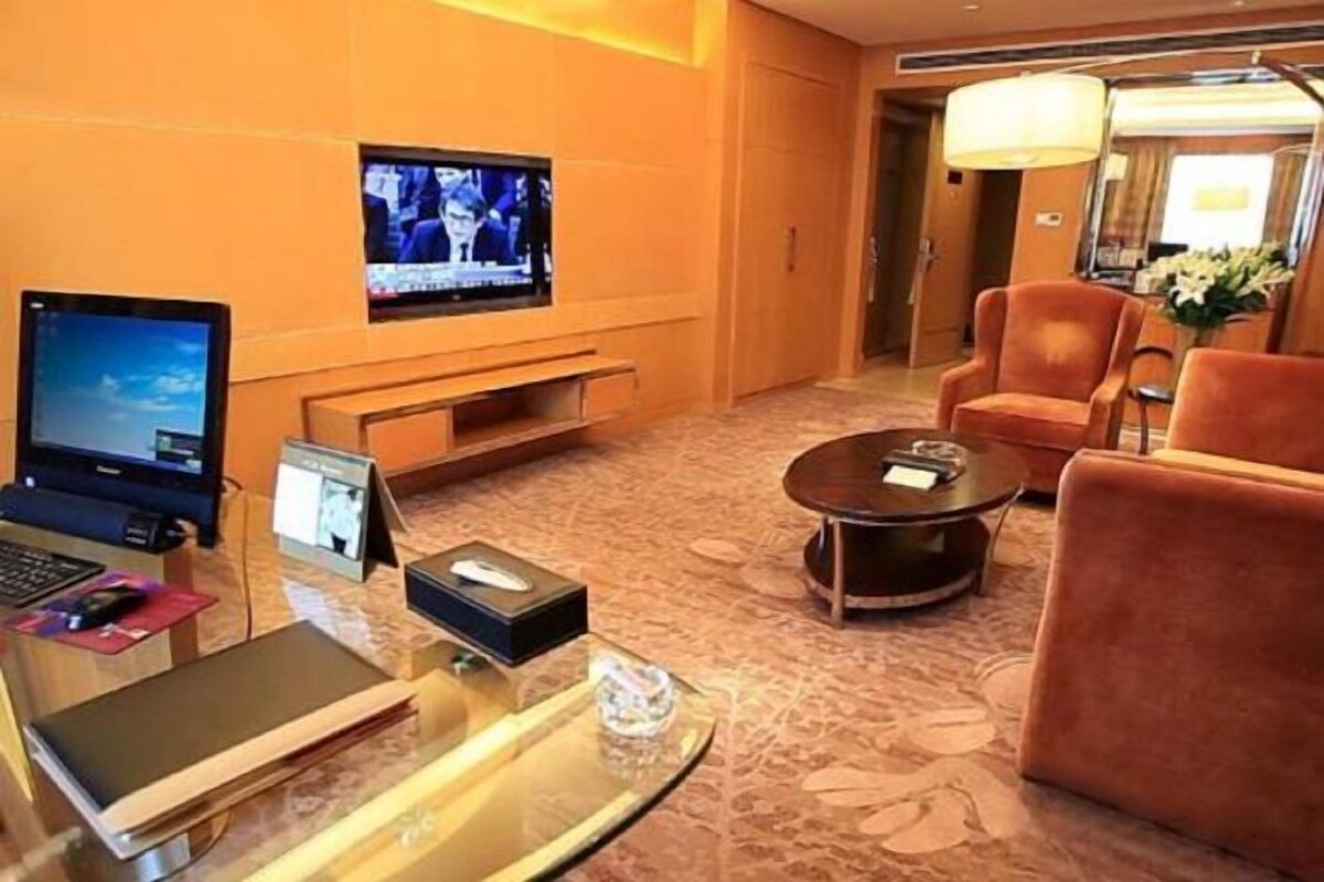 Un vestíbulo de hotel con mostrador de recepción, televisor, zona de estar y una lámpara decorativa.