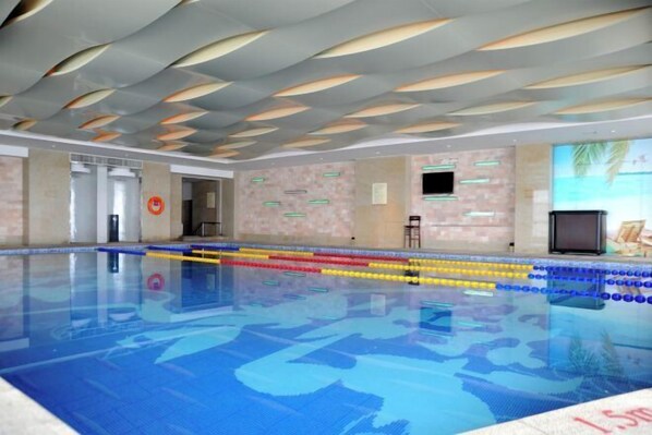 A swimming pool with lane dividers, a ceiling with wave-like patterns, and a wall with a screen displaying a beach scene. - Tiancheng Grand Hotel (Guangyuan City)