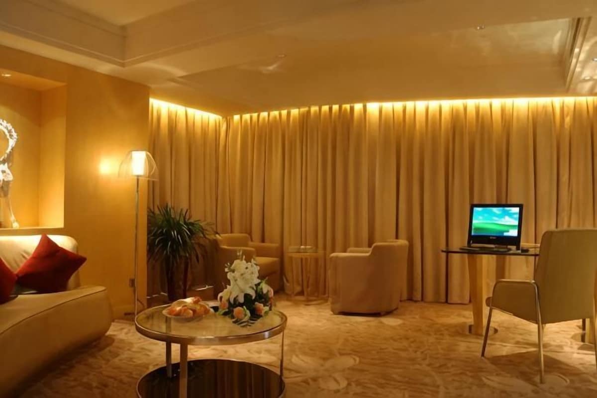 Une chambre d’hôtel avec un canapé, des fauteuils, une table basse, un téléviseur et un rideau en arrière-plan.