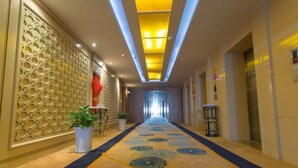 A hotel hallway with a patterned carpet, decorative wall panels, and a ceiling with recessed lighting. - Eyring Daqian International Hotel (Neijiang City)