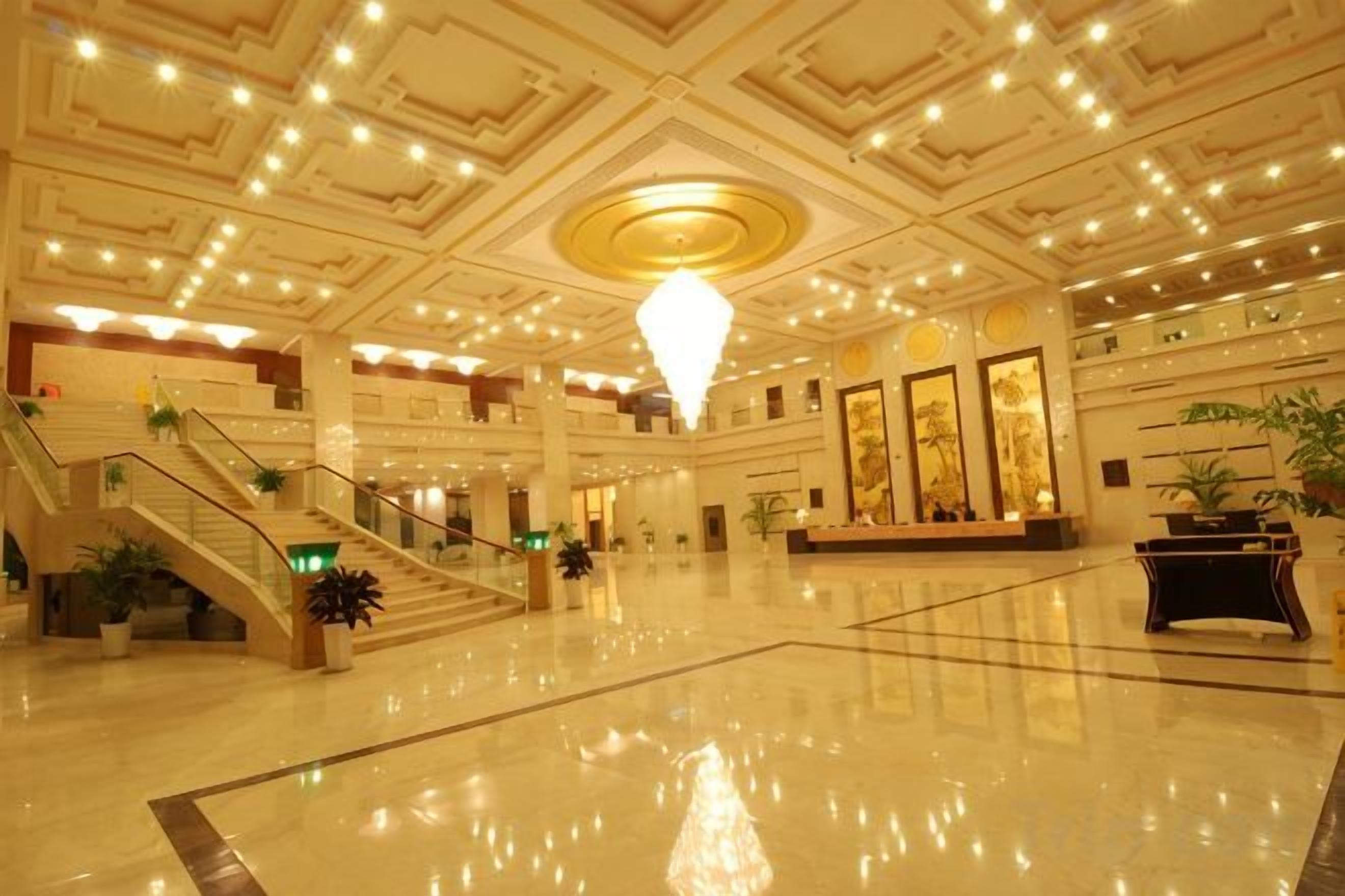 A spacious lobby with a grand staircase, a chandelier, and a polished floor.