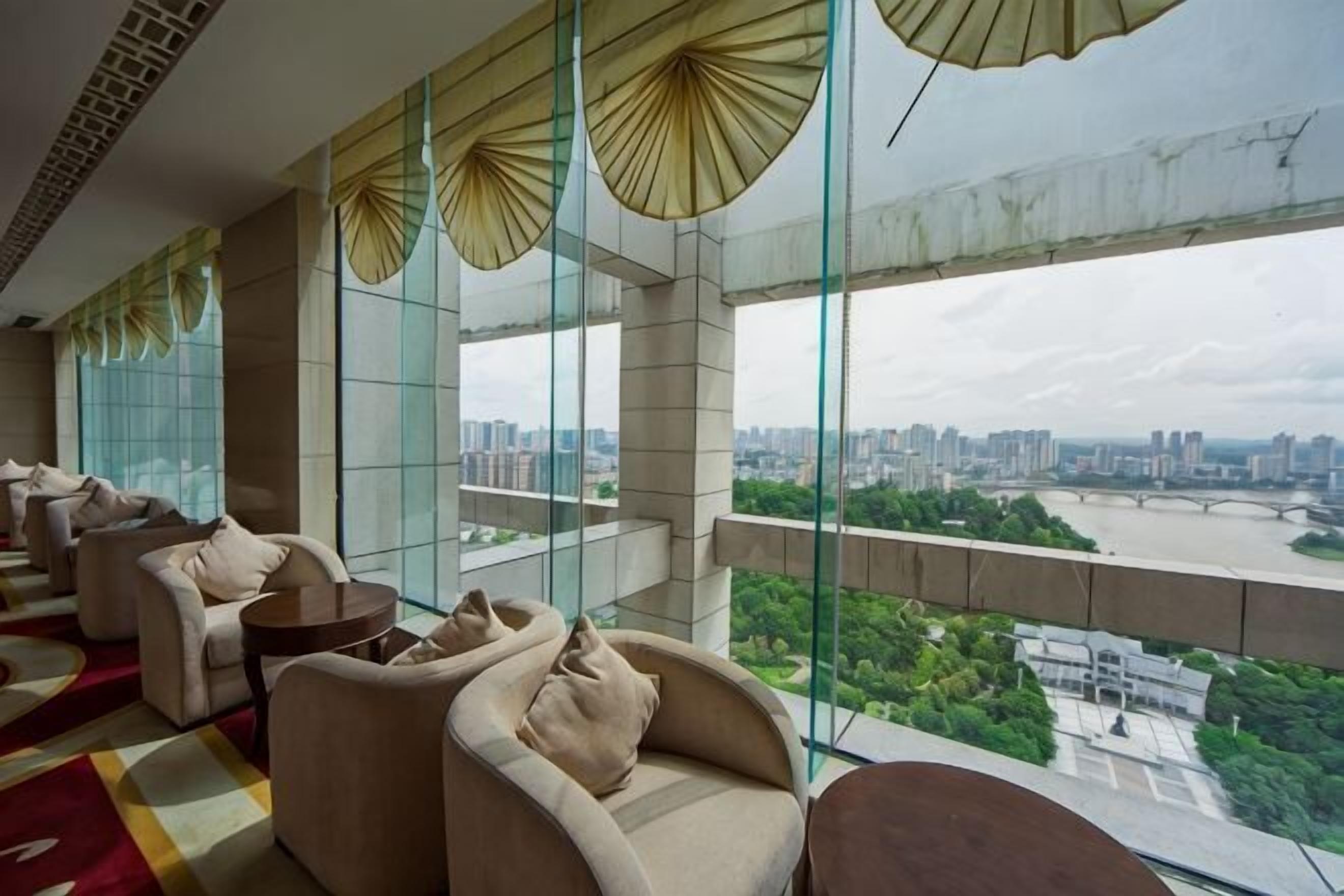 A hotel room with large windows, a city view, and a balcony with seating.