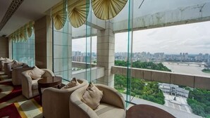 A hotel room with large windows, a city view, and a balcony with seating.