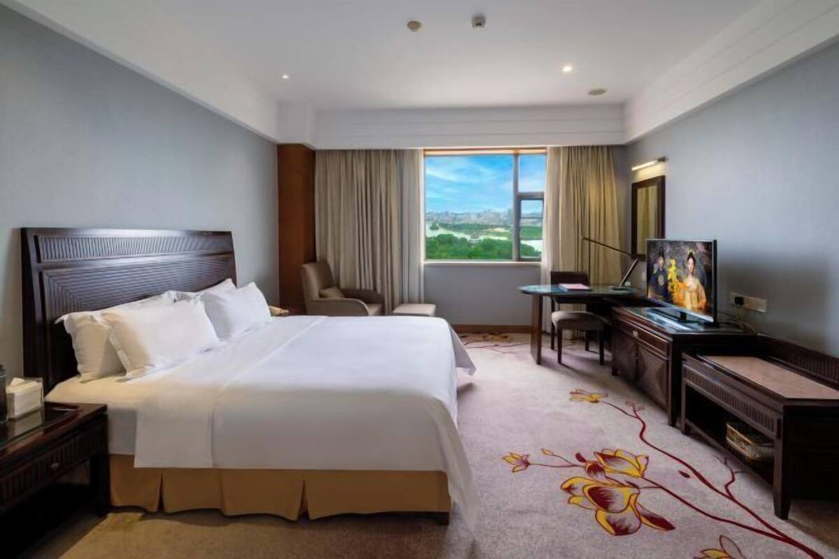 A hotel room with a large bed, a desk with a chair, a television, and a view of the outdoors.