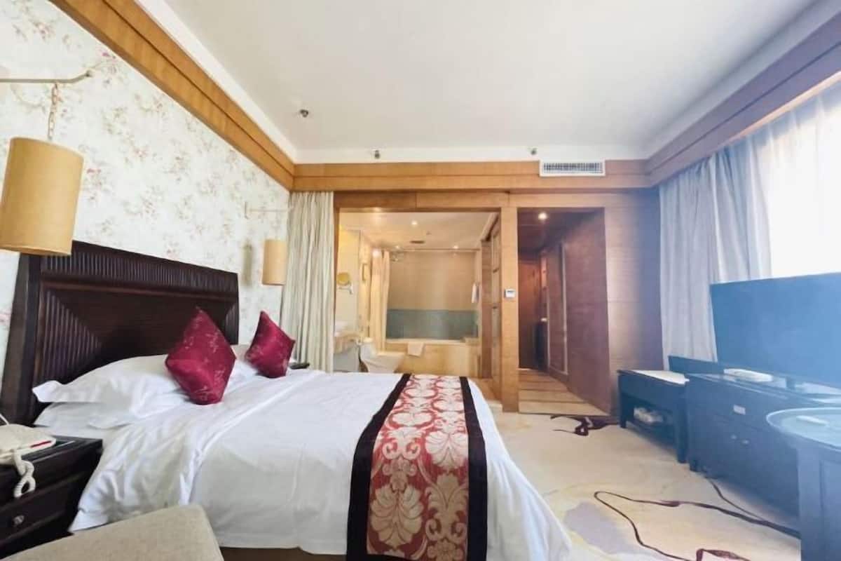 A hotel room with a bed, a desk, a television, and a bathroom visible through an open door.