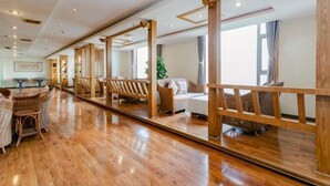 A spacious hotel room with wooden flooring, a large mirror, and a seating area with chairs and a sofa. - Eyring Daqian International Hotel (Neijiang City)