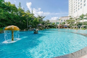 A swimming pool with a water feature, surrounded by palm trees and a hotel building.
