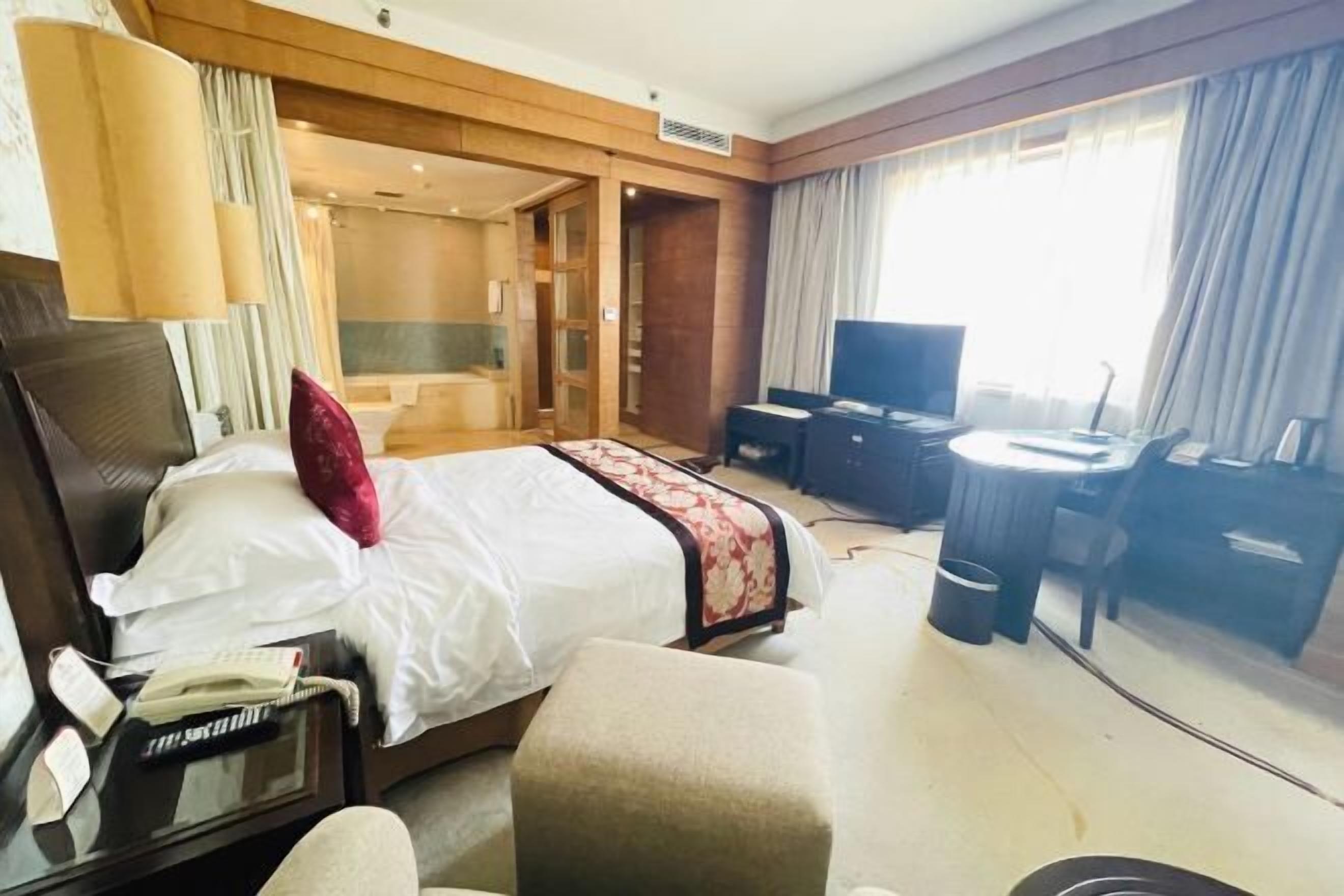 A hotel room with a bed, bedside table, lamp, TV, and a small desk with a chair.