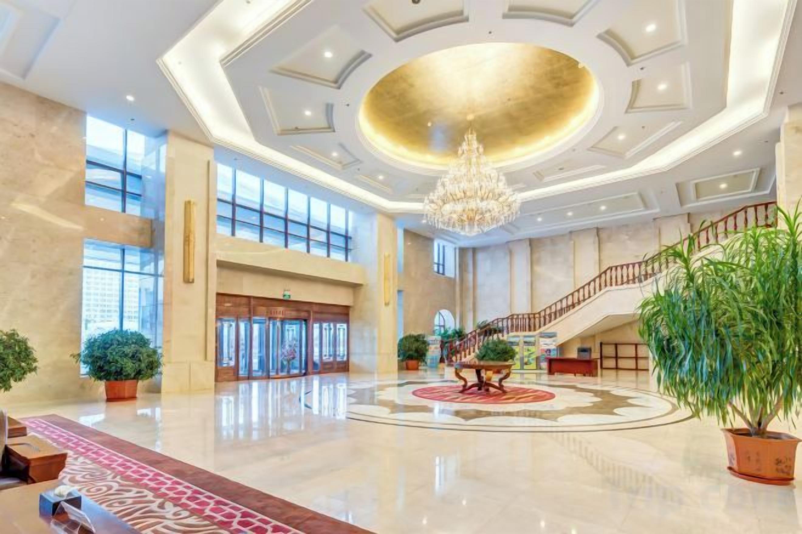 Un lobby amplio con una imponente lámpara de candelabro, una escalera y plantas en macetas.