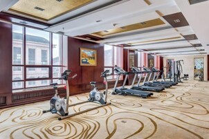 Un gimnasio de hotel con varias caminadoras y equipo de ejercicio, ventanas amplias y una alfombra estampada.