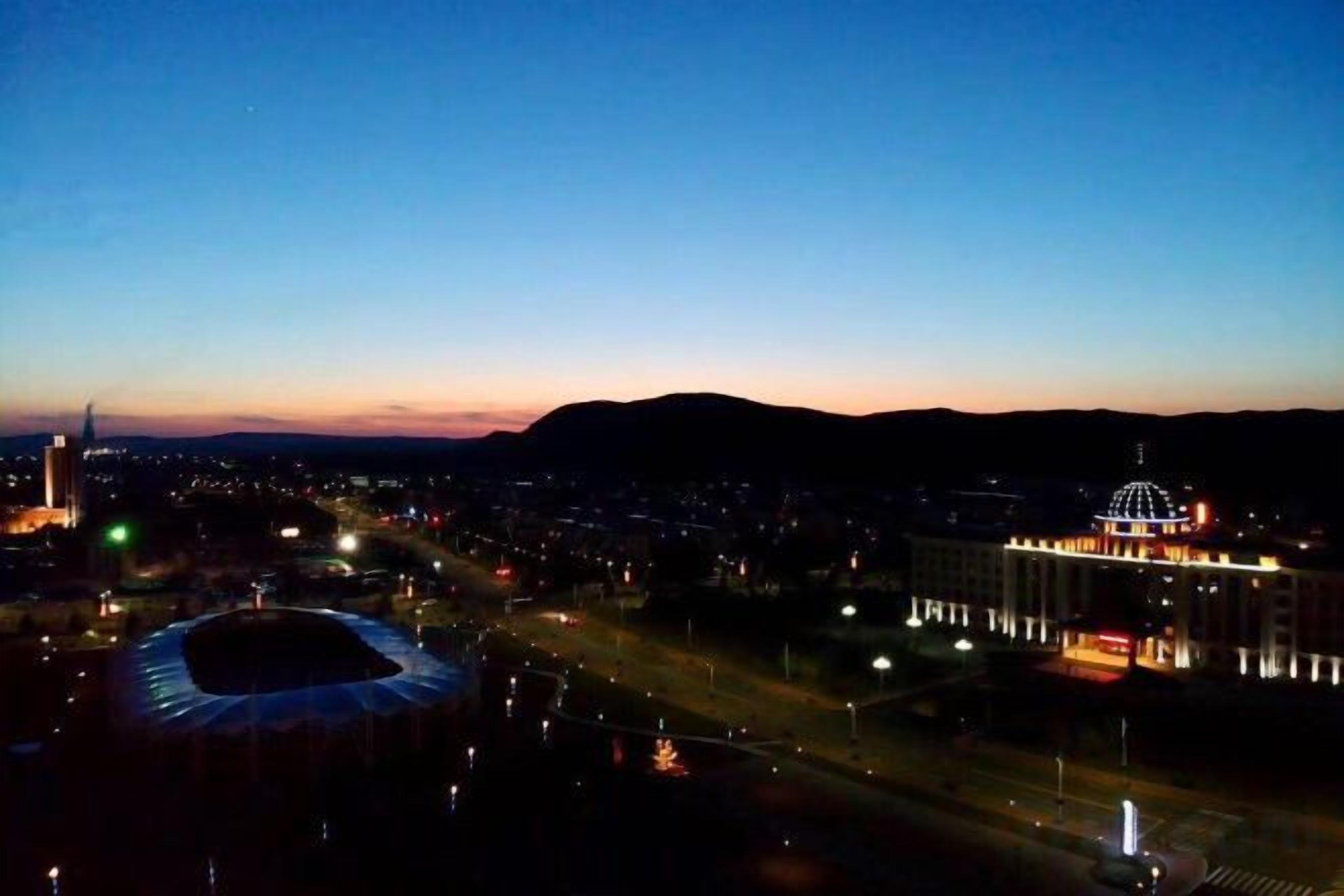 Une vue sur une ville au crépuscule, avec des bâtiments illuminés et un stade.