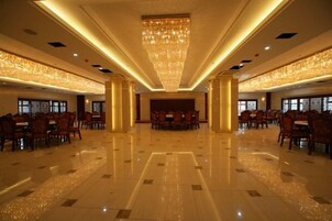 Un salón espacioso con techo alto, candelabros y filas de mesas y sillas.