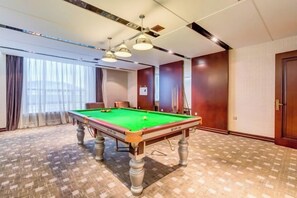 A pool table in a room with a patterned carpet, a ceiling light fixture, and a door. - Longyuan Northern Base (Yichun)