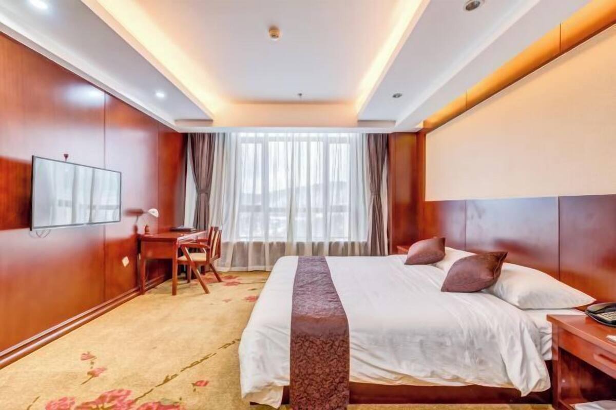 A hotel room with a bed, bedside table, and a desk with a chair.