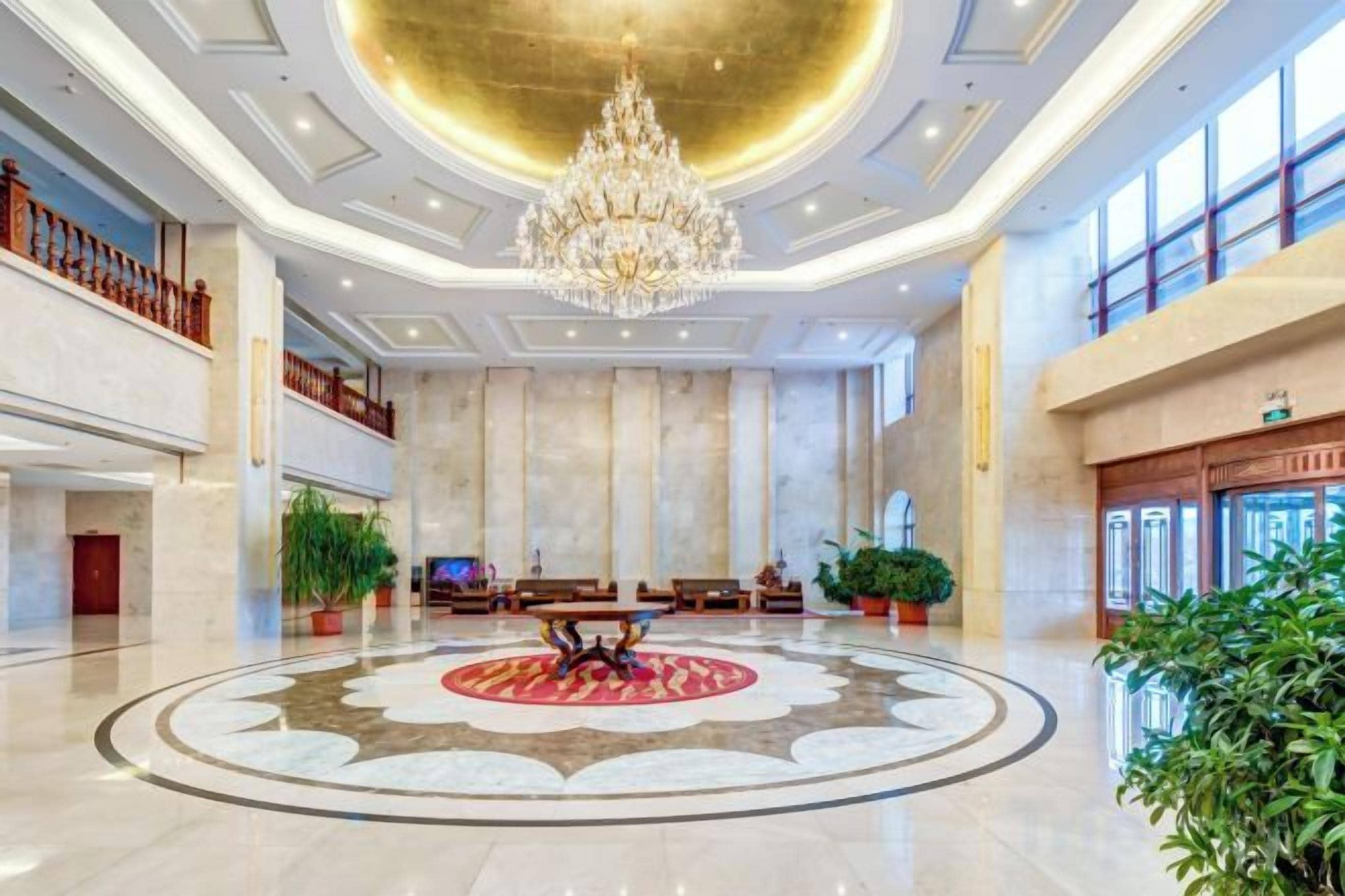 A spacious lobby with a grand chandelier, a central circular floor design, and a high ceiling.