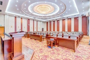 Un salón de conferencias con filas de sillas, un atril y suelo alfombrado.