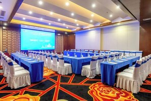 A conference room with rows of tables and chairs, a projection screen, and a carpeted floor.