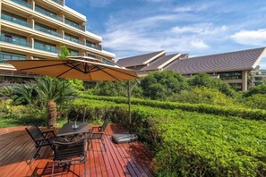 An outdoor patio with a table and chairs, surrounded by lush greenery and a large umbrella.
