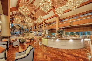 Um hall amplo com uma recepção central, diversas áreas de estar e um teto alto com luminárias detalhadas.