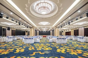 Un amplio salón de conferencias con mesas redondas, una alfombra estampada y un candelabro.