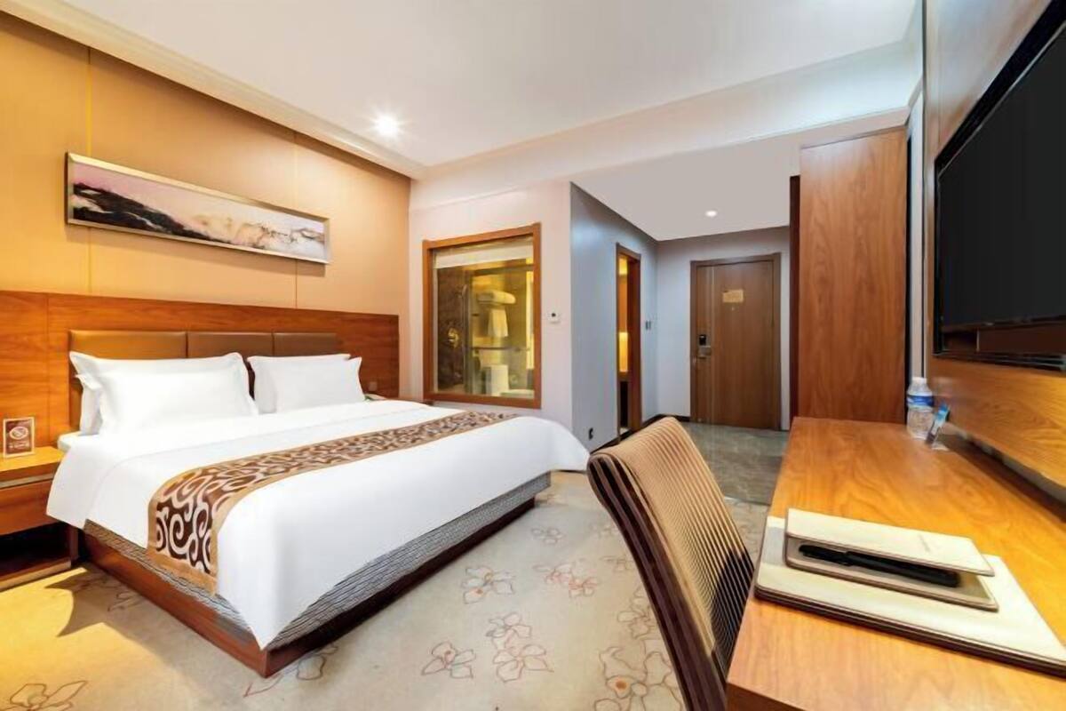 A hotel room with a bed, a desk, a chair, a television, and a bathroom door.