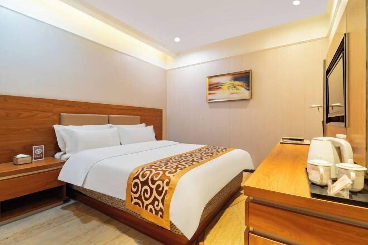 A hotel room with a bed, wooden headboard, bedside table, and a desk with a mirror.