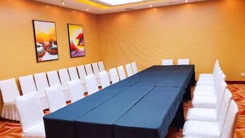Uma sala de conferências com uma mesa comprida, cadeiras brancas e duas obras de arte emolduradas na parede.