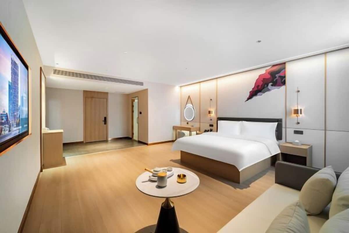 A modern hotel room with a large bed, bedside tables, a round coffee table, and a painting on the wall.