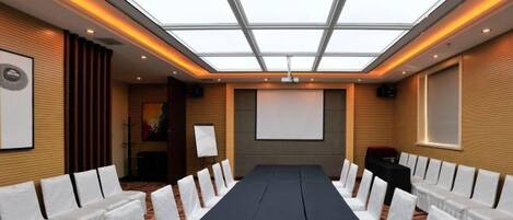 A conference room with a long table, white chairs, a projector screen, and a ceiling with a skylight.