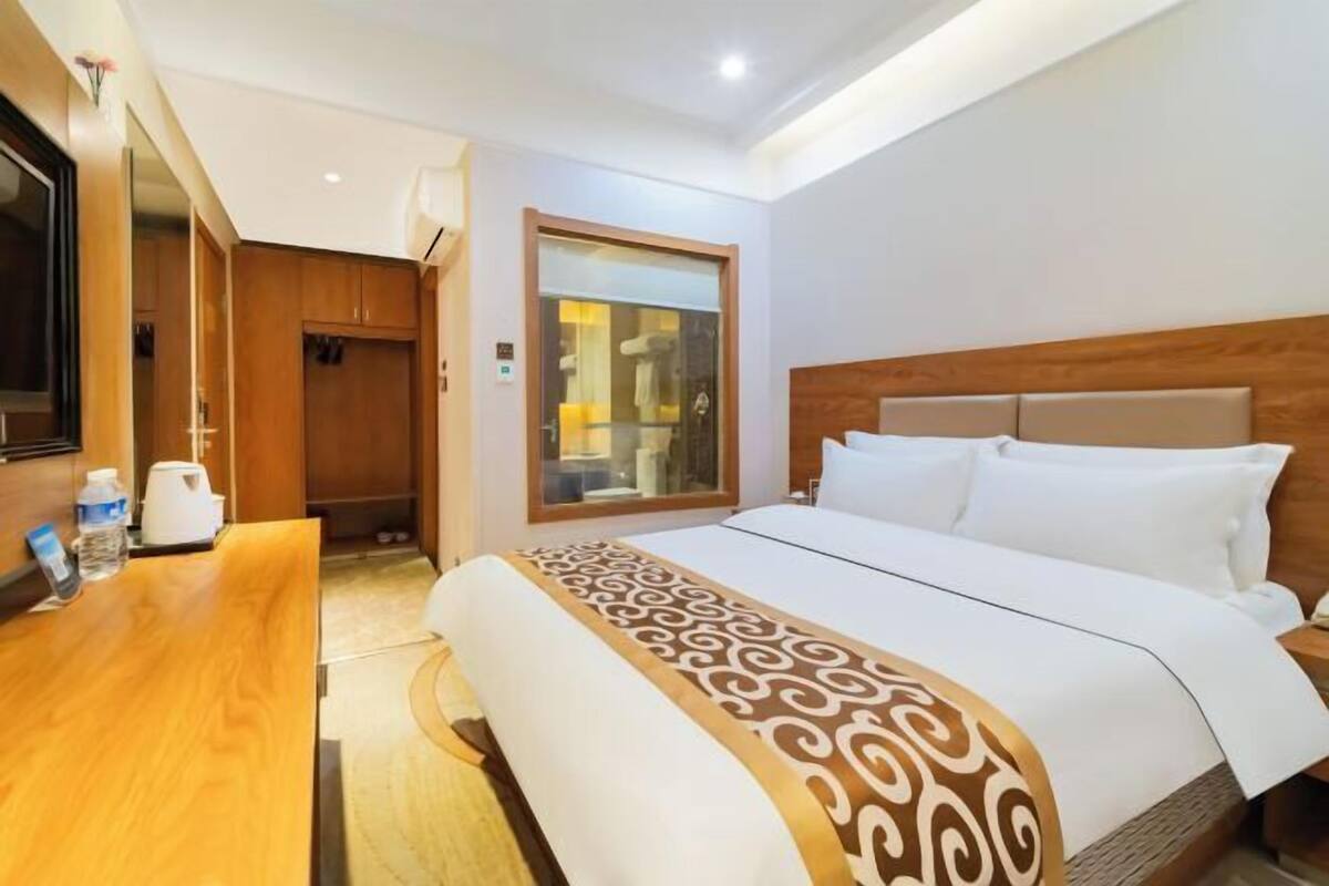 A hotel room with a large bed, a wooden headboard, a bedside table, and a mirror.
