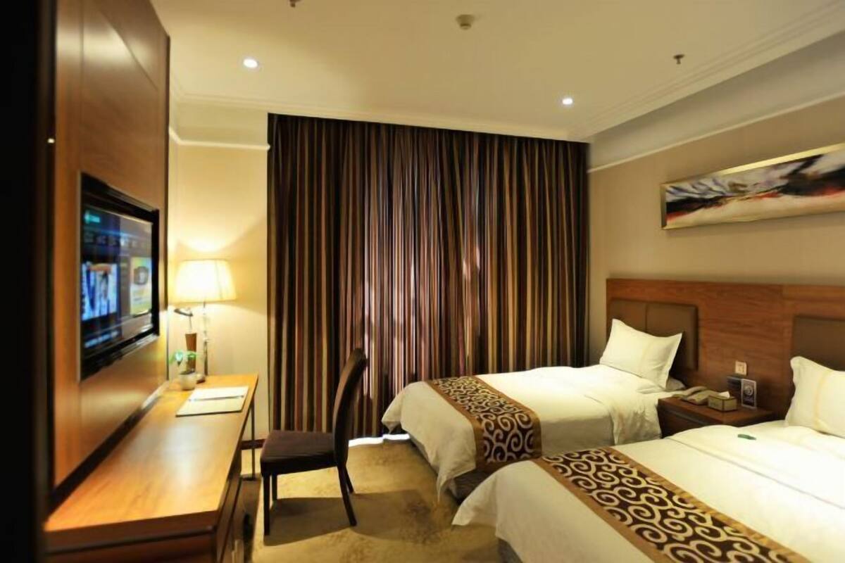 A hotel room with two beds, a desk, a TV, and a curtain.