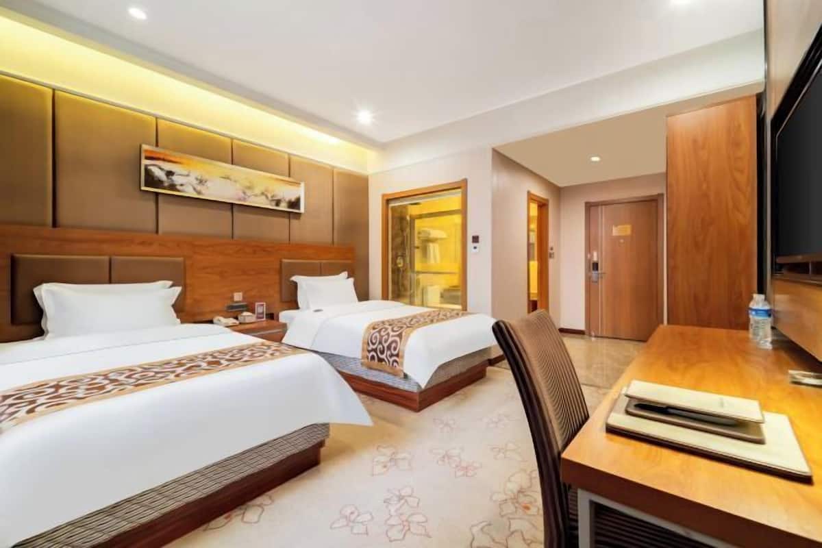 A hotel room with two beds, a wooden headboard, a flat-screen TV, a desk with a chair, and a bathroom door.