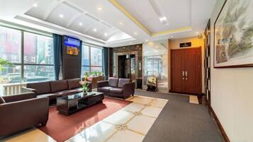 Een hotel lobby met een receptiebalie, een zithoek en een groot raam met uitzicht op de stad.