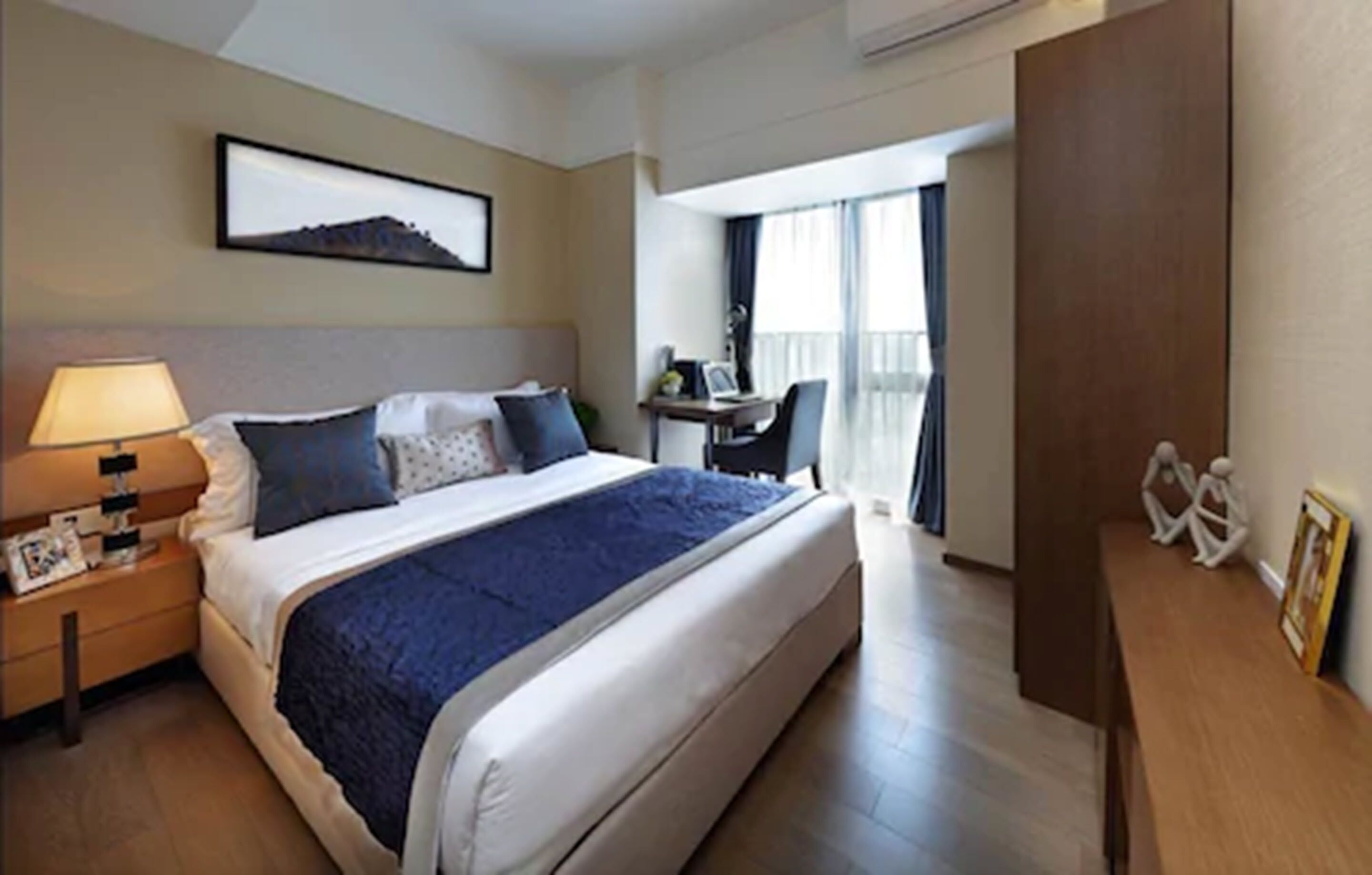 A hotel room with a bed, bedside table, lamp, and a desk with a chair.