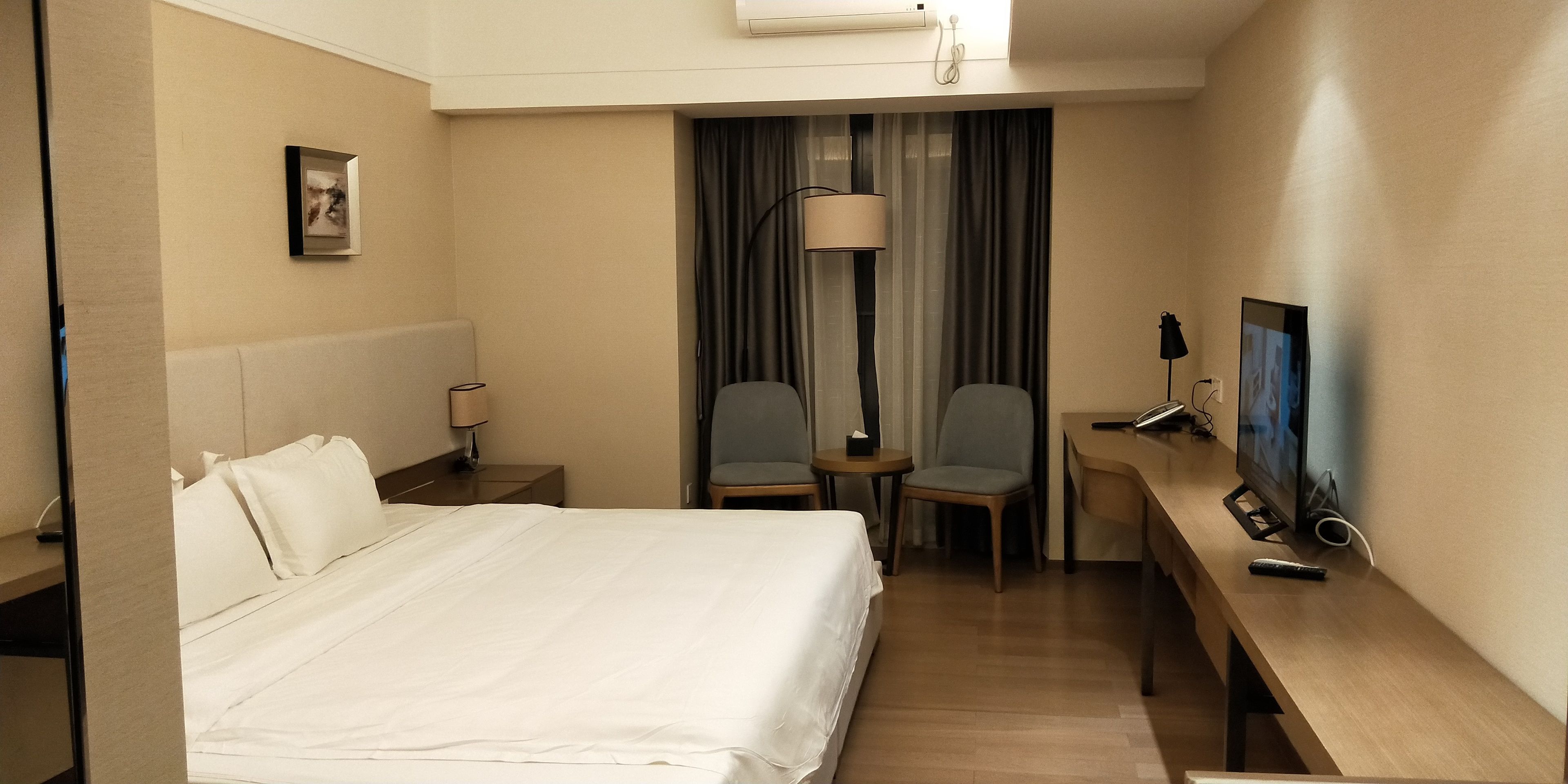 A hotel room with a bed, a desk, a chair, a TV, and a lamp.