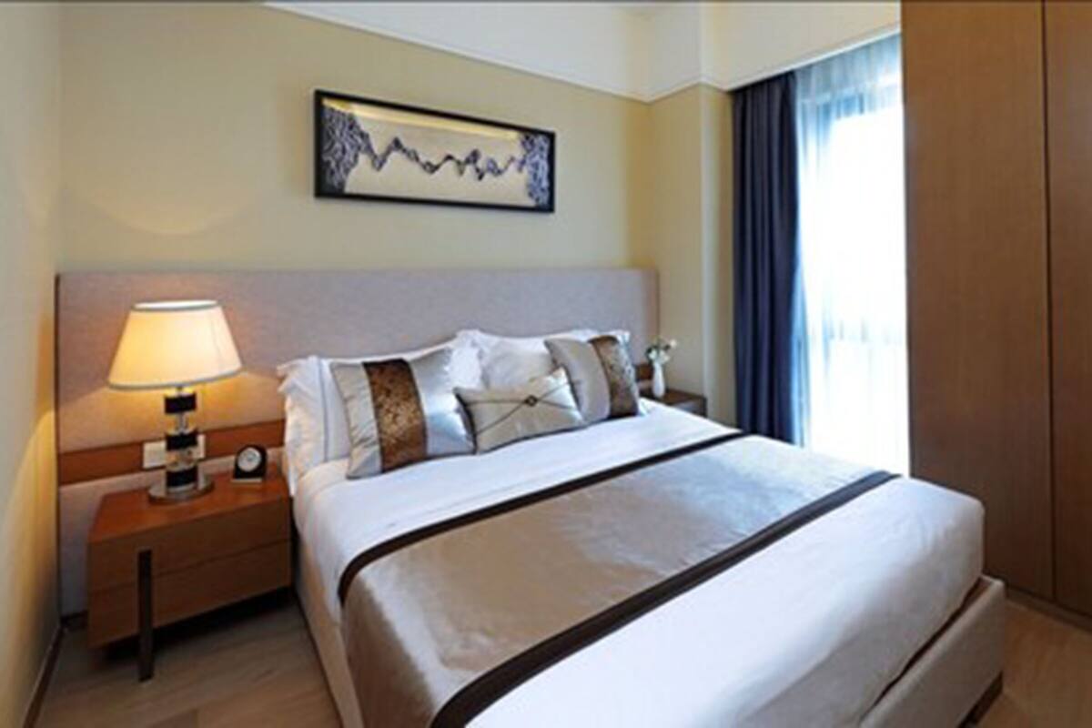 A hotel room with a bed, a nightstand with a lamp, a clock, and a framed artwork on the wall.