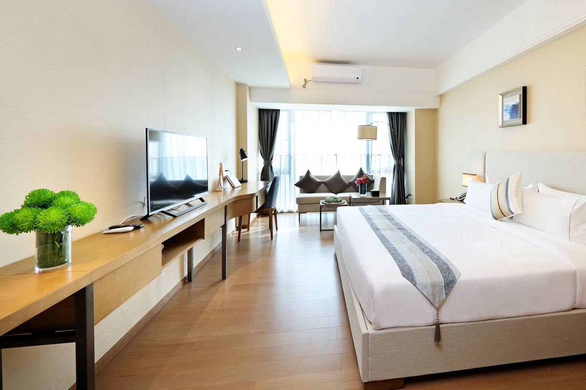 A hotel room with a large bed, a desk with a computer, a TV, and a view of the outdoors.