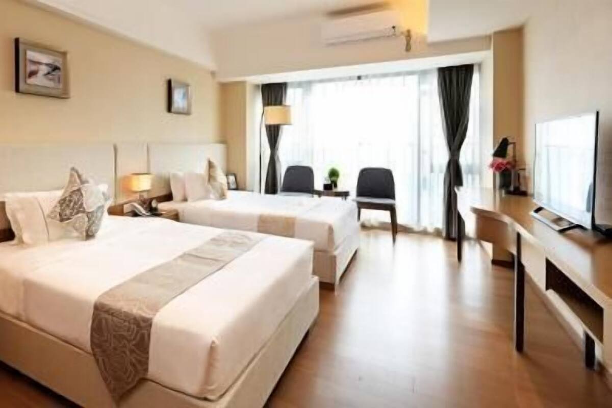 A hotel room with two beds, a desk, a chair, a TV, and a window with curtains.