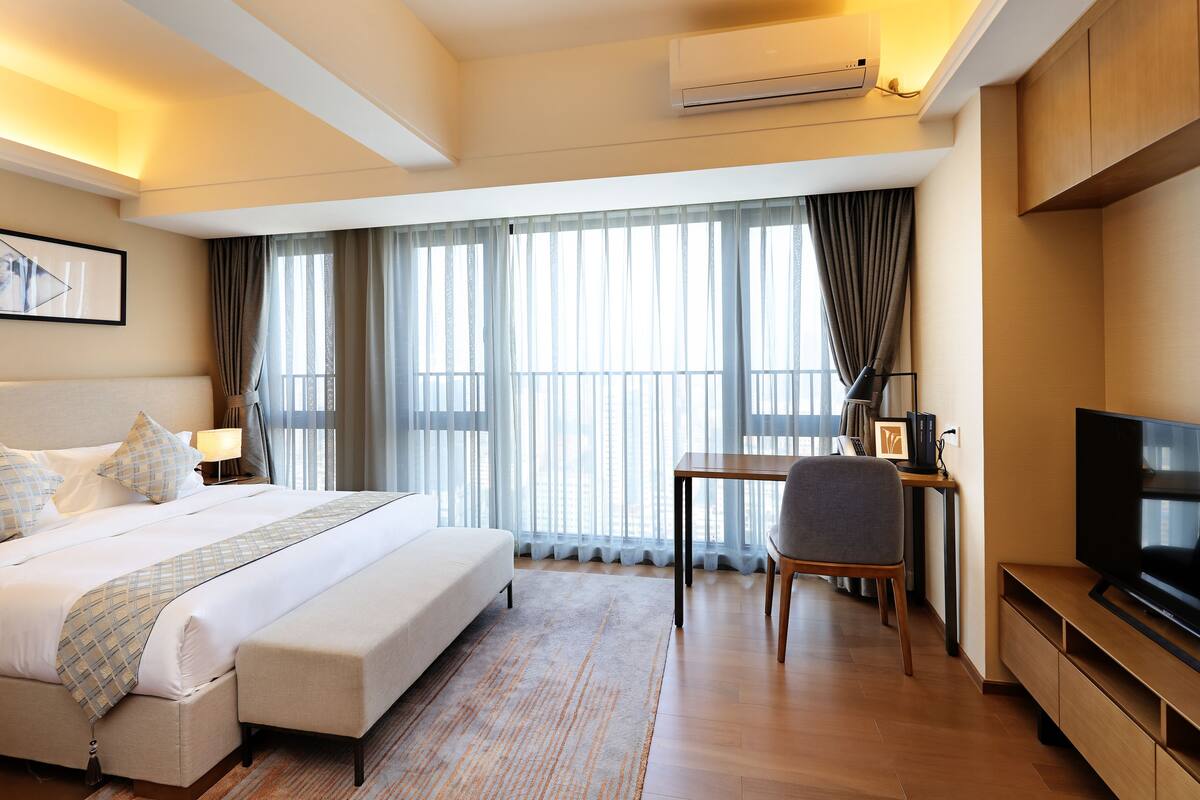 A hotel room with a large bed, a desk with a chair, a television, and a window with curtains.