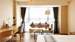 A hotel room with a bed, a desk, a chair, a sofa, a coffee table, and a window with curtains. - Yuwa Serviced ApartHotel (Foshan)
