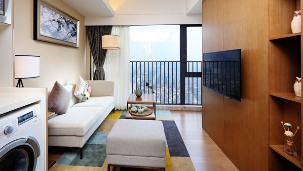 A modern living room with a sofa, ottoman, coffee table, and a washing machine. - Yuwa Serviced ApartHotel (Foshan)