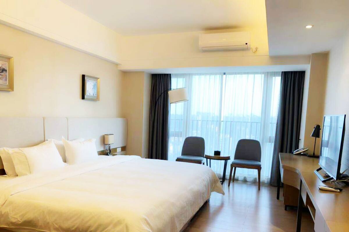 A hotel room with a large bed, two chairs, a desk with a TV, and a window with curtains.