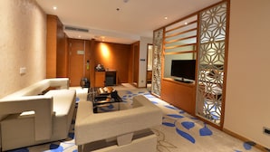 Habitación de hotel moderna con sofá, una mesita de café, televisor y un separador decorativo.