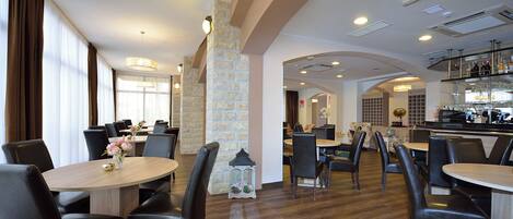 A hotel dining area with round tables, black chairs, and a stone pillar.