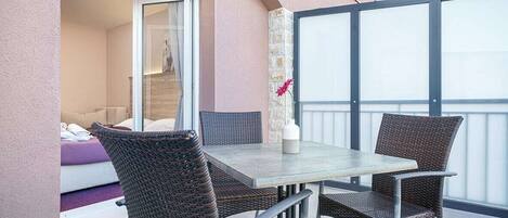 An outdoor balcony with a table and chairs, a sliding glass door leading to a room, and a flower vase on the table.