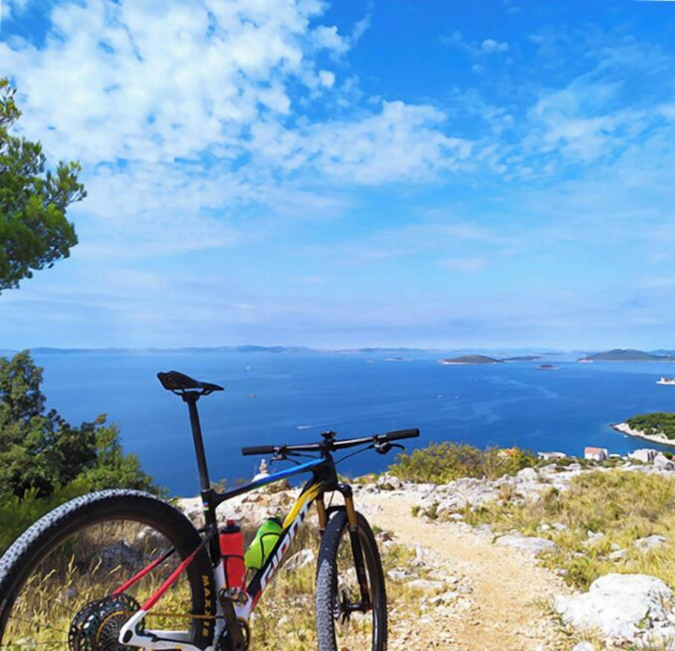 A mountain bike parked on a rocky path with a view of the sea and islands in the distance.