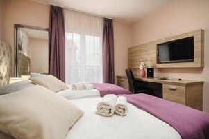 Habitación de hotel con dos camas, un escritorio, una silla, un televisor y un ventanal con cortinas.