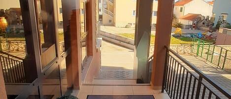 Entrada de hotel con piso de baldosas, una planta en maceta y felpudo con el nombre del hotel.