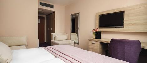 A hotel room with a bed, a desk, a chair, a TV, and a mirror.