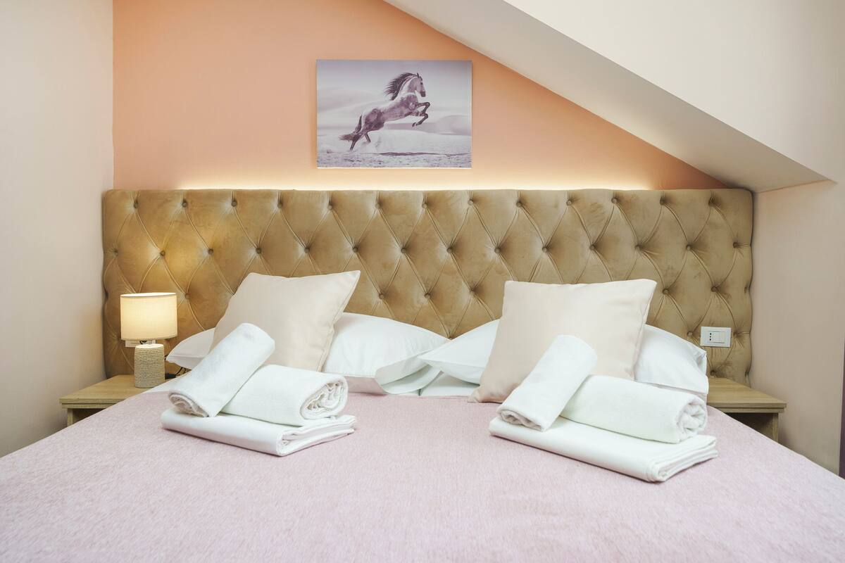 A neatly made bed with white linens and pillows, a bedside lamp, and a framed picture of a horse on the wall.
